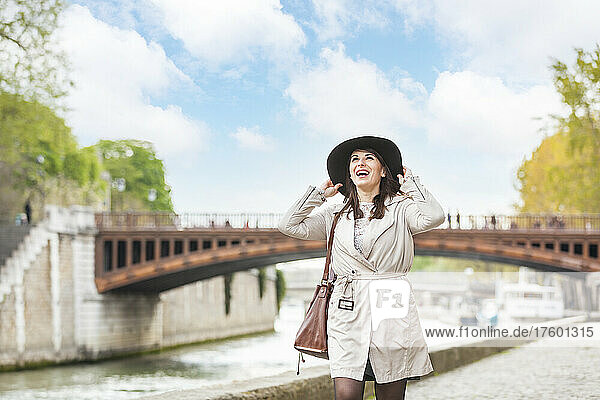 Happy woman with hat walking on footpath by Seine river