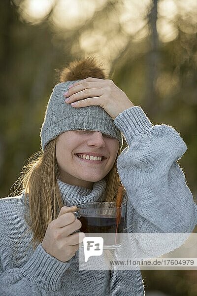 Porträt einer jungen Frau im Winter mit Mütze  lachen  wärmt sich an einer Tasse Tee  im Wald  Oberbayern  Bayern  Deutschland  Europa