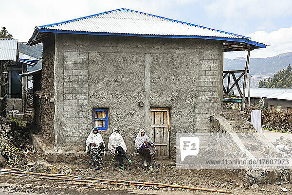 Drei Menschen sitzen vor der Tür eines Hauses im Hochland von Äthiopien; Äthiopien
