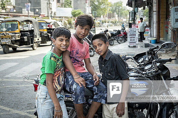 Drei Jungen versammeln sich auf einer Straße um ein Motorrad und schauen in die Kamera; Amritsar  Punjab  Indien
