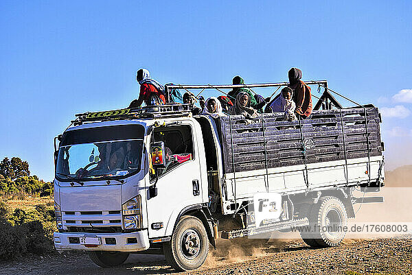 Menschen stehen auf der Ladefläche eines Lastwagens  der auf einer staubigen  unbefestigten Straße im ländlichen Äthiopien fährt; Äthiopien