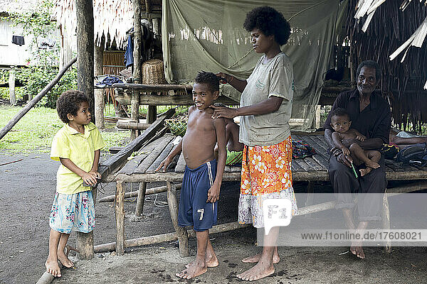 Junge  der von seiner Mutter die Haare geschnitten bekommt  während ein Familienmitglied zuschaut  Fergusson-Insel  D'Entrecasteaux-Inseln  Papua-Neuguinea; Fergusson-Insel  Milne Bay-Provinz  Papua-Neuguinea
