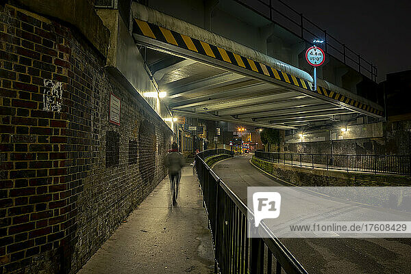 Fußgänger  der nachts unter einer Straßenbrücke in der Nähe von Haggerston auf dem Bürgersteig geht; London  England
