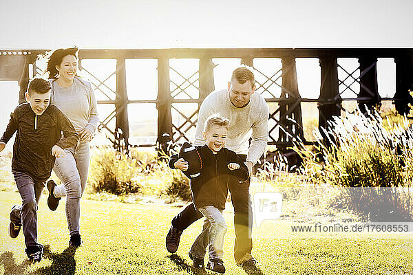 Family chasing young son in a game of football on a beautiful autumn day in a city park; St. Alberta  Alberta  Canada
