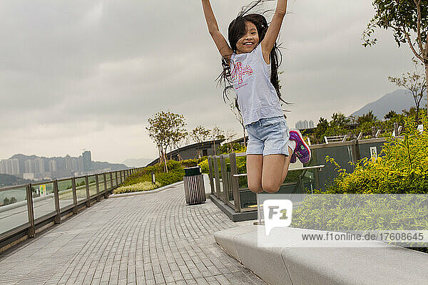 Mädchen  das auf einem Gehweg am Kai Tak Cruise Terminal in die Luft springt; Hongkong  China