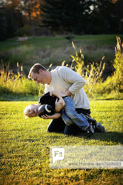 Vater und kleiner Sohn toben auf dem Rasen in einem Stadtpark; St. Albert  Alberta  Kanada