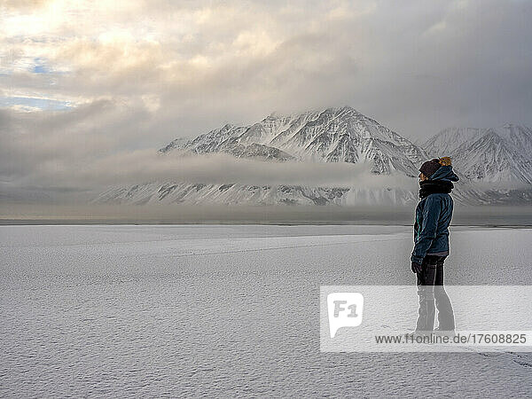 Woman standing on the frozen shoreline of Kathleen Lake looking out at the moody landscape; Haines Junction  Yukon  Canada
