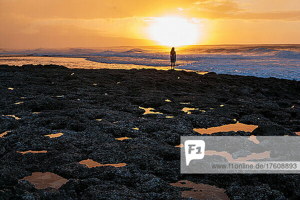 Eine junge Frau beobachtet vom Rocky Point aus die Wellen und den Sonnenuntergang.