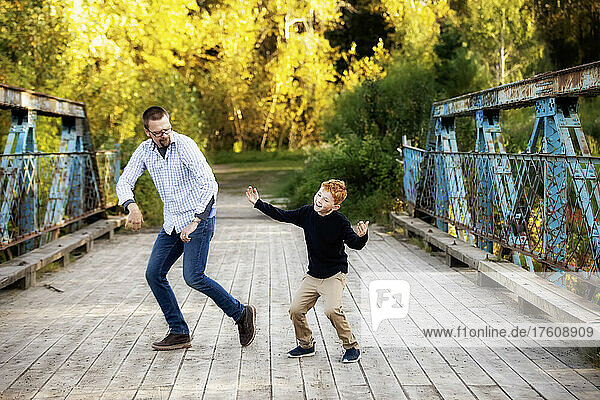Father and son doing dance moves on a bridge in a park in autumn; Edmonton  Alberta  Canada