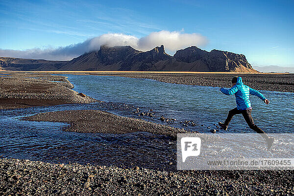 Ein Mann springt über einen Bach an der Südküste Islands.