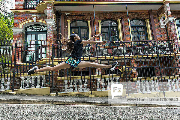 Mädchen springt in der Luft vor einem Gebäude in einem öffentlichen Park; Hongkong  China