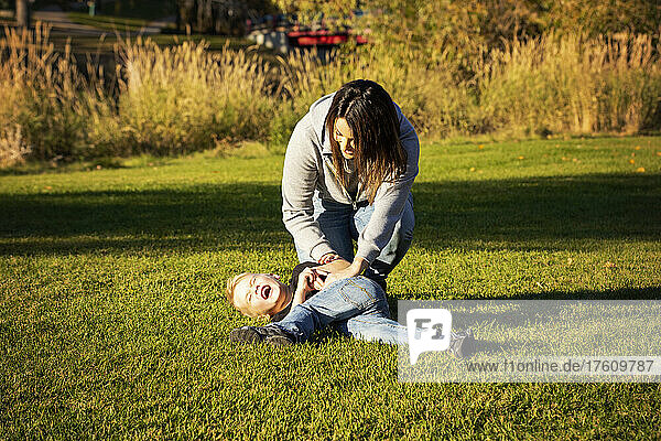 Mutter und kleiner Sohn toben auf dem Rasen eines Stadtparks; St. Albert  Alberta  Kanada