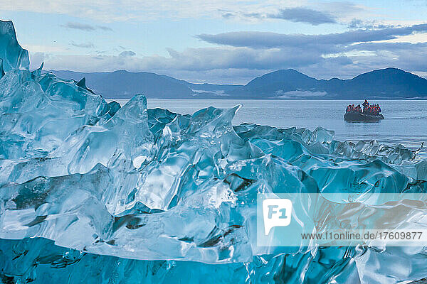 Ein Schlauchboot mit Touristen hinter einem blauen Eisberg.