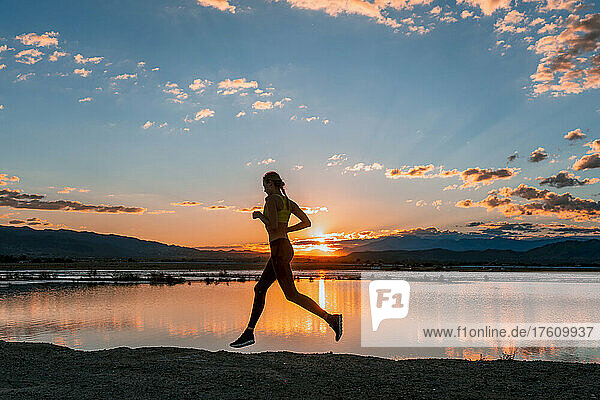A woman runs along Sunfair dry lake bed at sunset.