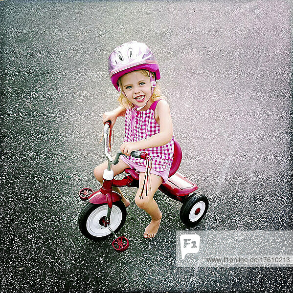 A two year old girl rides her ride tricycle on a summer's day.; Cabin John  Maryland  United States.
