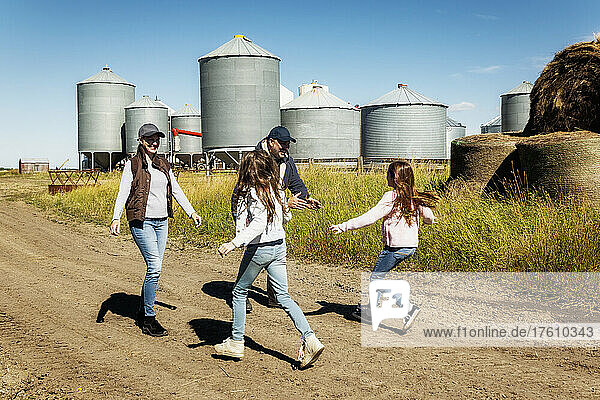 Zwei junge Mädchen  die ihren Eltern auf der Familienfarm entgegenlaufen  mit Getreidespeichern im Hintergrund; Alcomdale  Alberta  Kanada