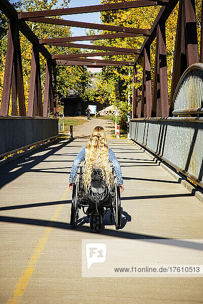 Junge querschnittsgelähmte Frau mit langen blonden Haaren  die an einem schönen Herbsttag in ihrem Rollstuhl über eine Brücke fährt; Edmonton  Alberta  Kanada