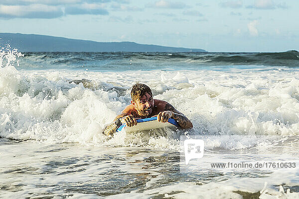 Nahaufnahme eines Mannes  der auf einem Bodyboard eine Welle in den Strand von D. T. Fleming Beach reitet  mit der Insel Molokai im Hintergrund; Kapalua  Maui  Hawaii  Vereinigte Staaten von Amerika