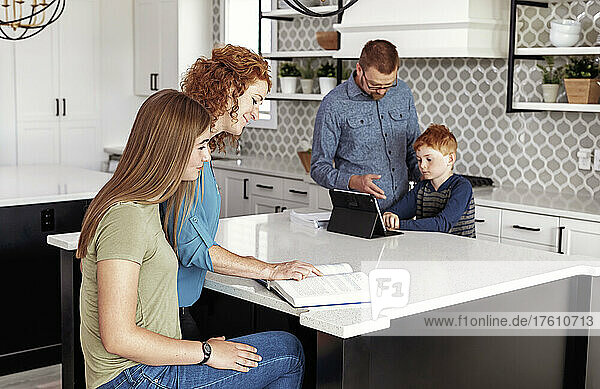 Eltern helfen ihrem Sohn und ihrer Tochter im Teenageralter bei den Hausaufgaben in der heimischen Küche; Edmonton,  Alberta,  Kanada