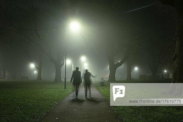 Bewegungsunschärfe und Silhouette von zwei Personen  die an einem nebligen Morgen in London Fields  Shoreditch  London  UK  spazieren gehen; London  England