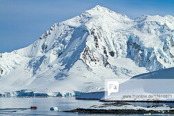 A zodiac from a cruise ship dwarfed by ice-covered mountains.