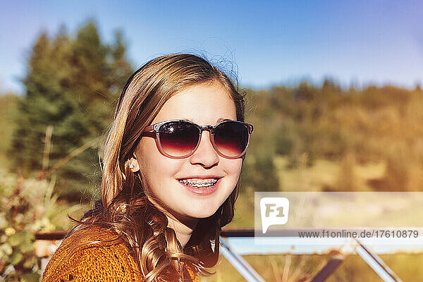 Outdoor portrait of a teenage girl with sunglasses and braces smiling at the camera in a park in autumn; Edmonton  Alberta  Canada