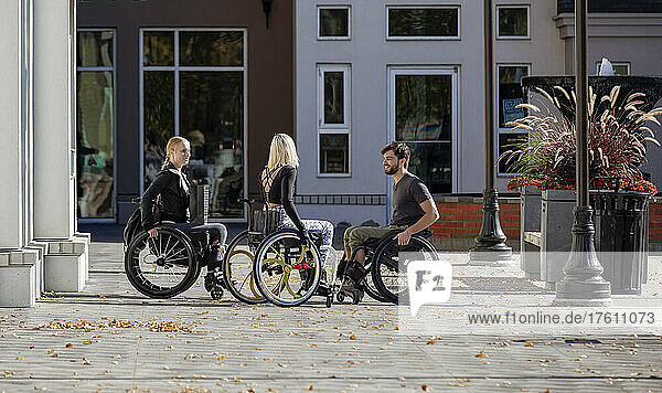 Drei junge querschnittsgelähmte Freunde unterhalten sich draußen auf einem Gehweg in einem Stadtgebiet; Edmonton  Alberta  Kanada