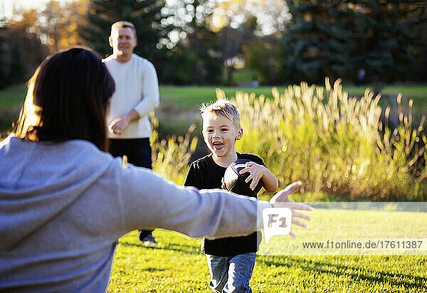 Young family plays in the park together with a football on a beautiful autumn day; St. Albert Alberta  Canada