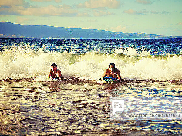 Glückliches Ehepaar spielt in den Wellen mit Bodyboards am D. T. Fleming Beach  mit der Insel Molokai im Hintergrund; Kapalua  Maui  Hawaii  Vereinigte Staaten von Amerika