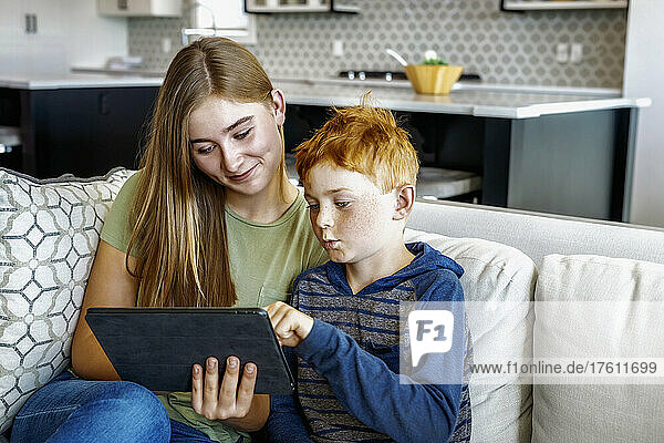 Ein Bruder und eine Schwester sitzen zu Hause auf einer Couch mit einem Tablet und schauen gemeinsam etwas an; Edmonton  Alberta  Kanada