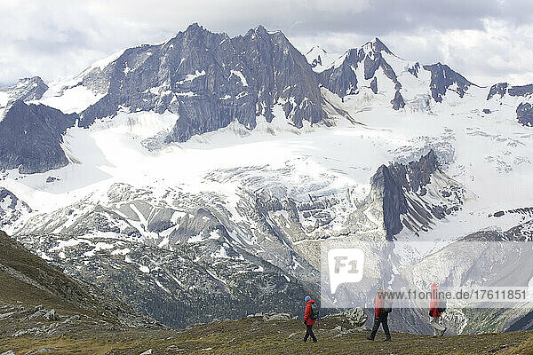 Hikers on a ridge line with snow covered peaks in the background; Adamants Mountain Range  British Columbia  Canada