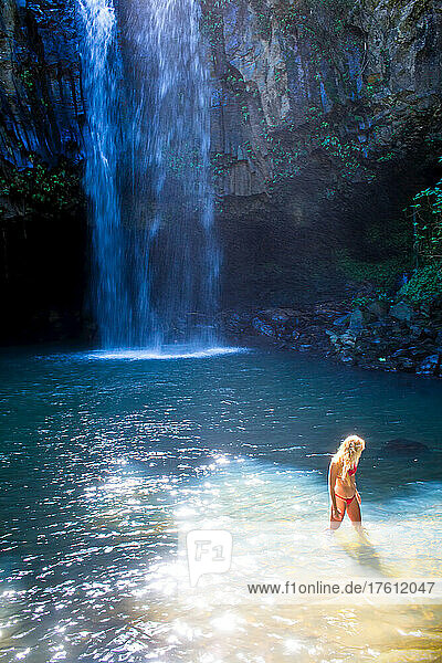 Eine junge Frau in einem natürlichen Becken am Fuße eines Wasserfalls.