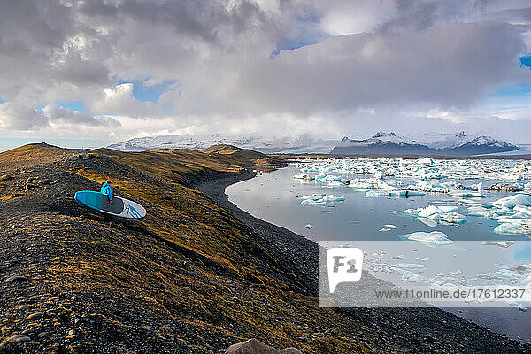 Ein Mann  der mit einem Paddleboard zur Gletscherlagune Jokulsarlon hinunterfährt.