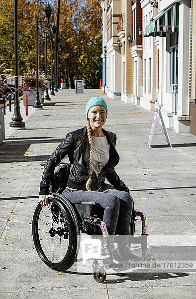 Junge querschnittsgelähmte Frau in ihrem Rollstuhl auf einem städtischen Gehweg an einem schönen Herbsttag; Edmonton  Alberta  Kanada