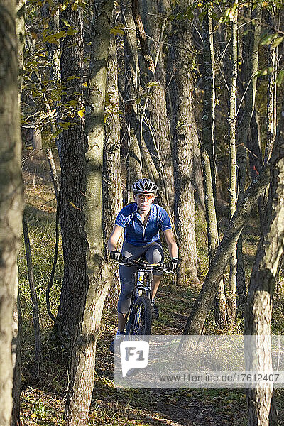 Woman mountain biker rides downhill through woods.; Seneca State Park  Gaithersburg Maryland.
