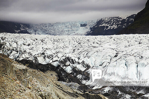 Distant hikers dwarfed by a massive Icelandic glacier.; Svinafellsjokull Glacier  Skaftafell National Park  Iceland.