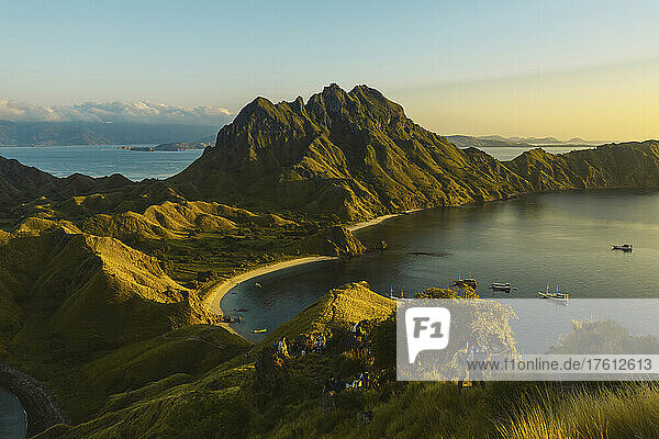 Travelers on hilltop watching the sunset with boats moored in the bay at Padar Island in Komodo National Park in the Komodo Archipelago; East Nusa Tenggara  Indonesia