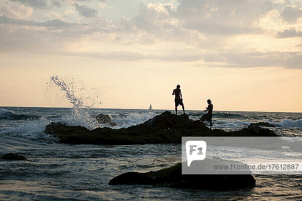 Männer beim Fischen vor den Felsen bei Sonnenuntergang.