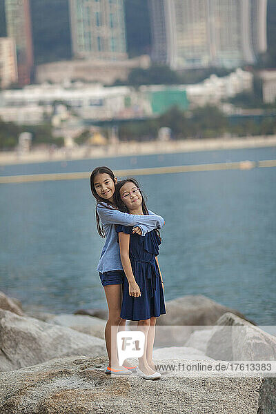Junge Schwestern stehen in einer Umarmung auf Felsbrocken in der Repulse Bay in Hongkong; Hongkong  China