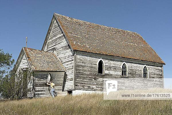 Woman looking in the window of an old abandoned church in the ghost town of Neidpath  Saskatchewan; Neidpath  Saskatchewan  Canada