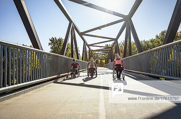 Drei junge querschnittsgelähmte Freunde verbringen Zeit miteinander  indem sie an einem schönen Tag in einem Stadtpark in ihren Rollstühlen über eine Parkbrücke fahren; Edmonton  Alberta  Kanada