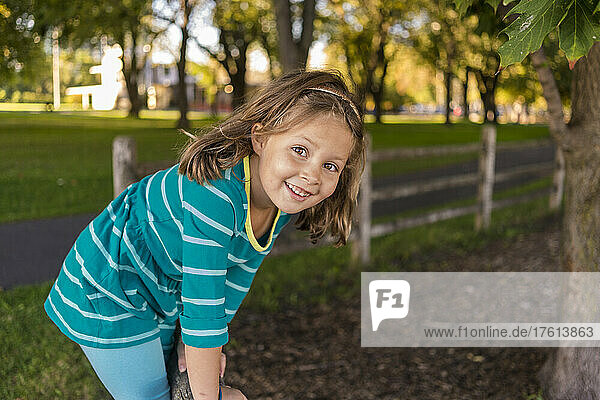 Portrait of a young girl standing on a rail fence in a park area looking at the camera; Toronto  Ontario  Canada