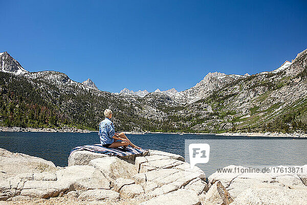 A woman sits by an alpine lake in the Sierra Nevadas.