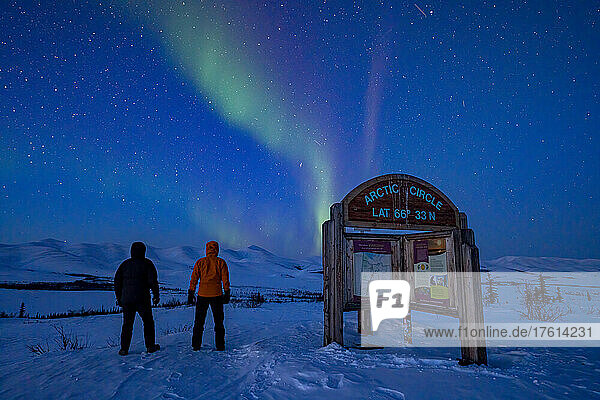 Blick von hinten auf zwei Personen  die das Polarlicht über dem Dempster Highway am Nachthimmel an der Grenze zum Polarkreis beobachten; Yukon  Kanada