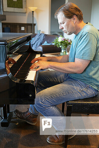 Mature man playing his grand piano at home; Kelowna  British Columbia  Canada