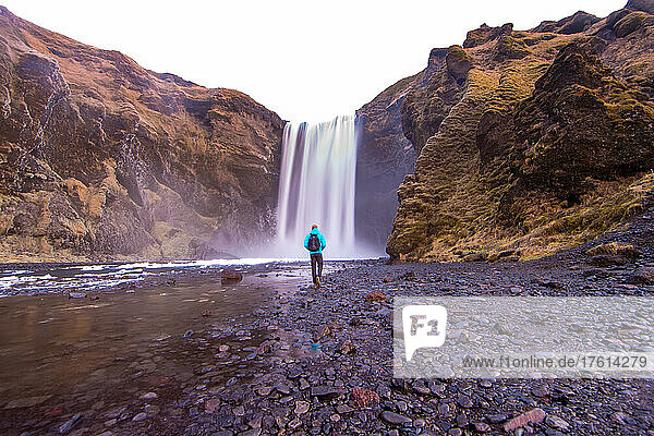 Ein Mann geht zum Skogafoss-Wasserfall in Island.