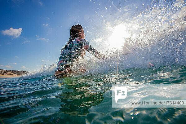 A surfer lets a wave pass by her while waiting for the right wave to ride and gets splashed
.