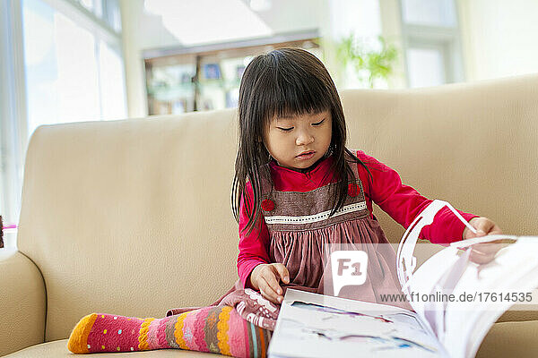 Young girl sits on a couch reading a storybook; Hong Kong  China