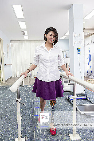 Young woman with leg prosthesis in therapy  walking with handrails; Bangkok  Thailand