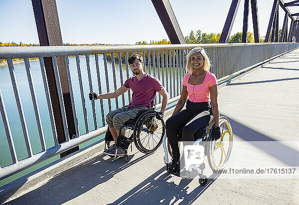 Zwei junge querschnittsgelähmte Freunde verbringen Zeit miteinander  indem sie sich an einem schönen Tag in einem Stadtpark in ihren Rollstühlen über eine Parkbrücke bewegen; Edmonton  Alberta  Kanada